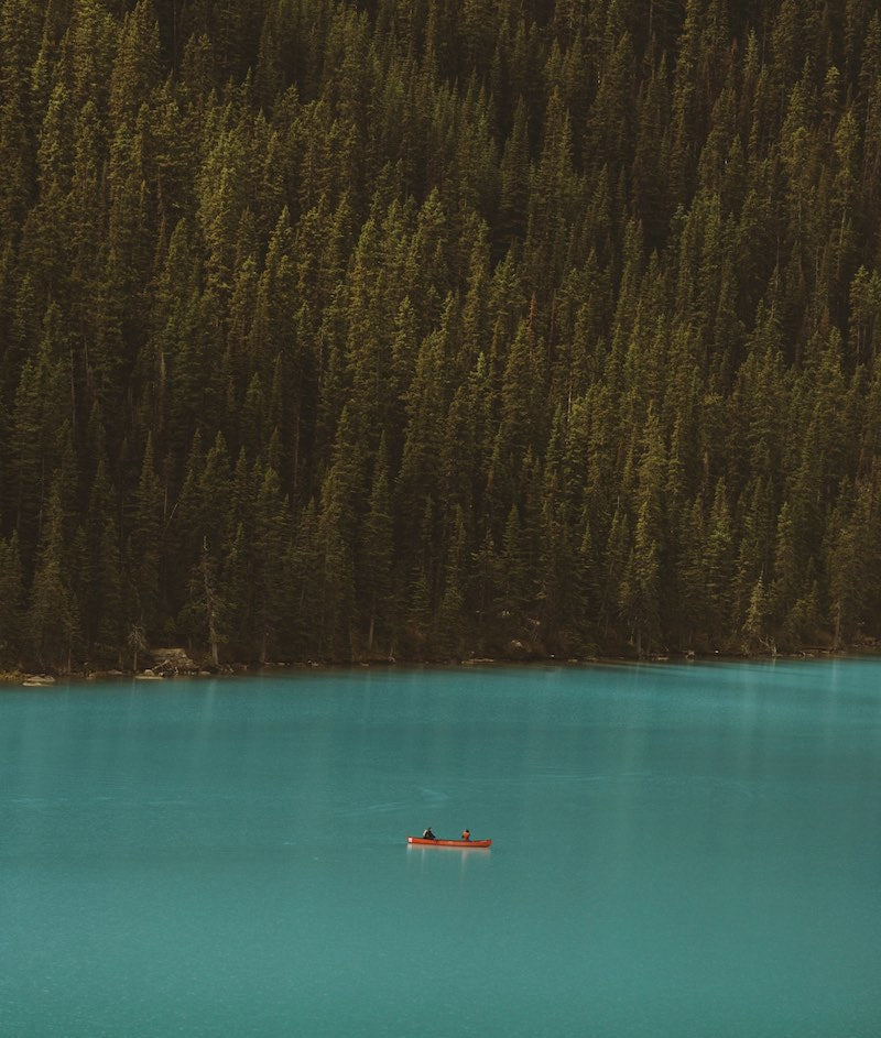 Canoeing in an emerald lake on a hillside with pine trees.