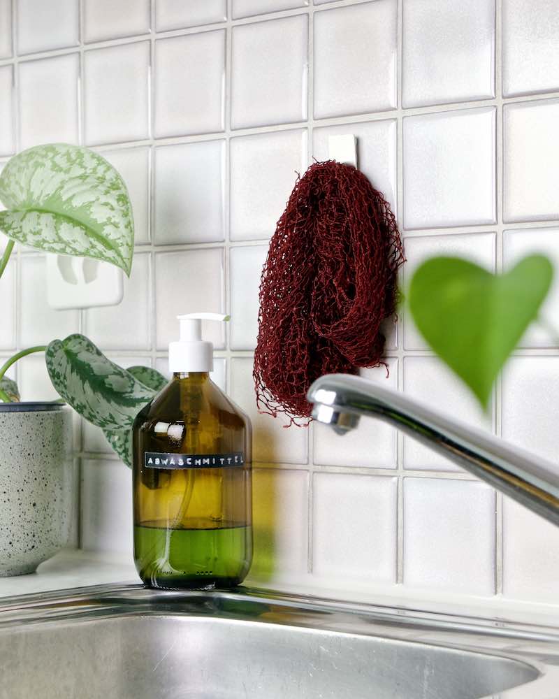 The Fischnetz dish sponge alternative is hanging on a kitchen wall over a kitchen sink.